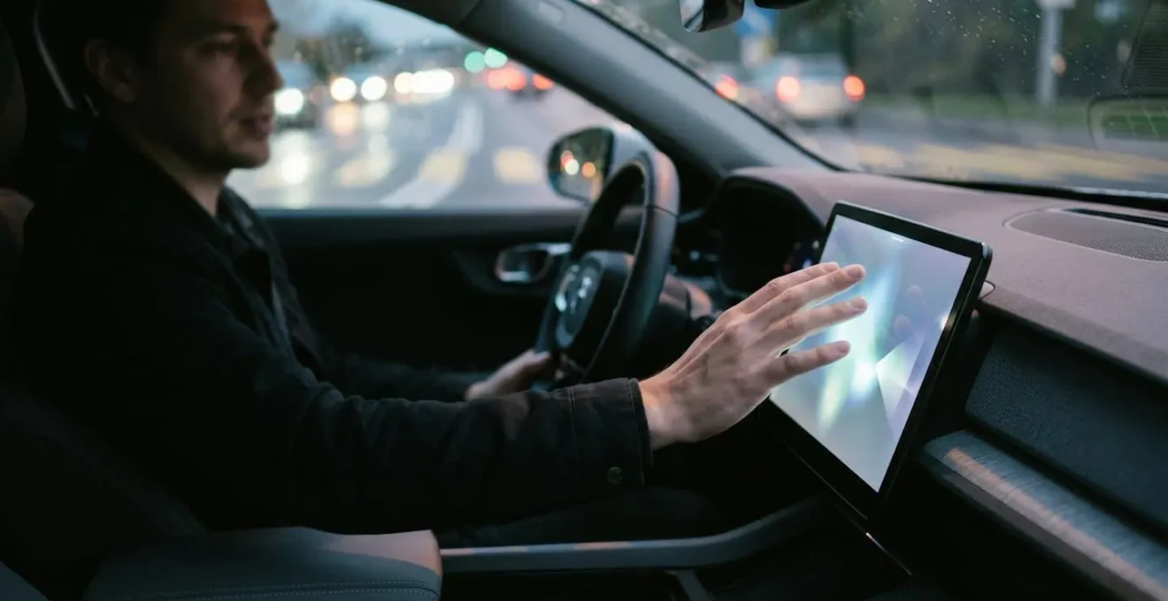 Driver's hand reaching toward car infotainment touchscreen while driving, illustrating modern vehicle control distraction