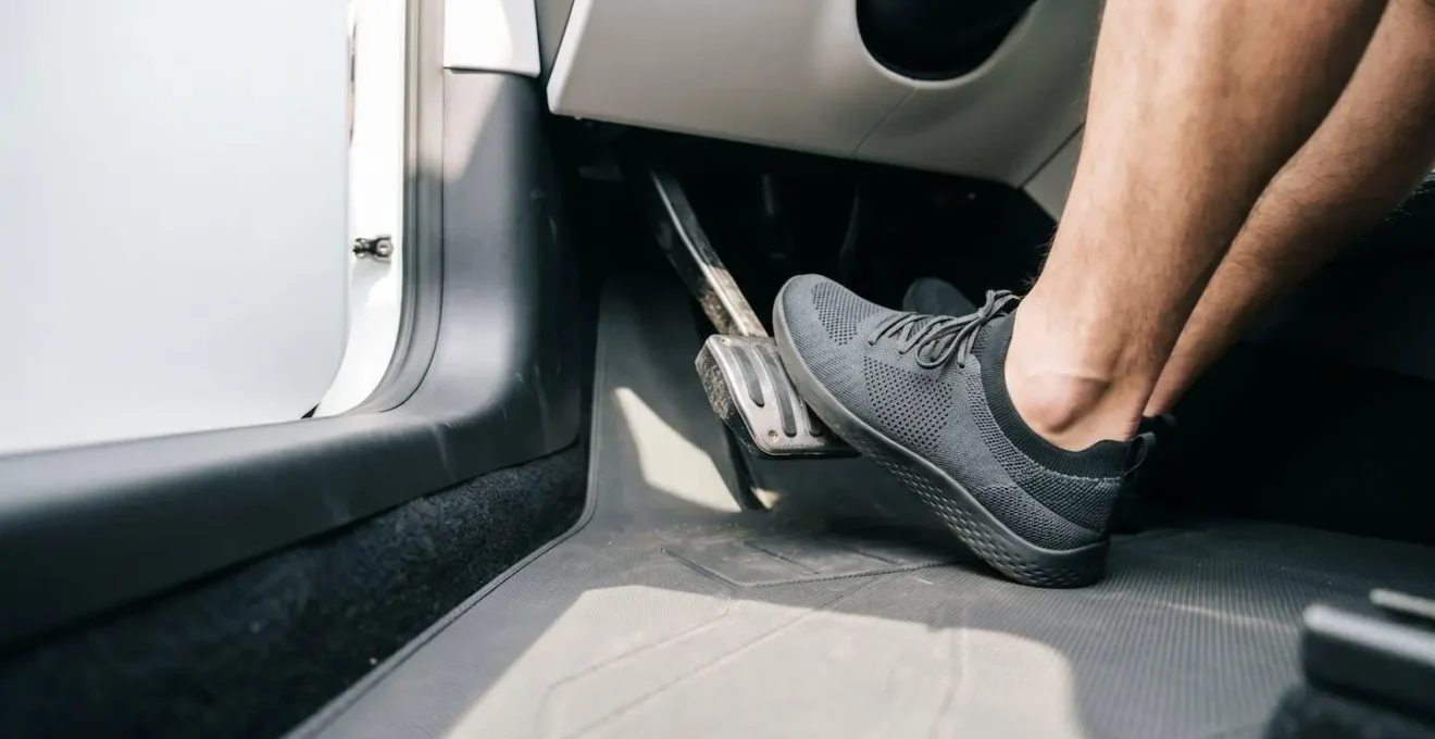 Wide-angle view of driver's foot applying firm pressure to brake pedal during emergency maneuver in modern vehicle interior