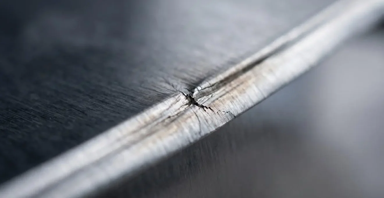 A macro close-up of a creased metal sheet, showing how a single fold line creates a point of structural failure and stress.