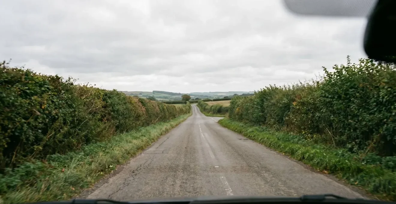 Driver perspective view of narrow British B-road with faded lane markings and tight corners