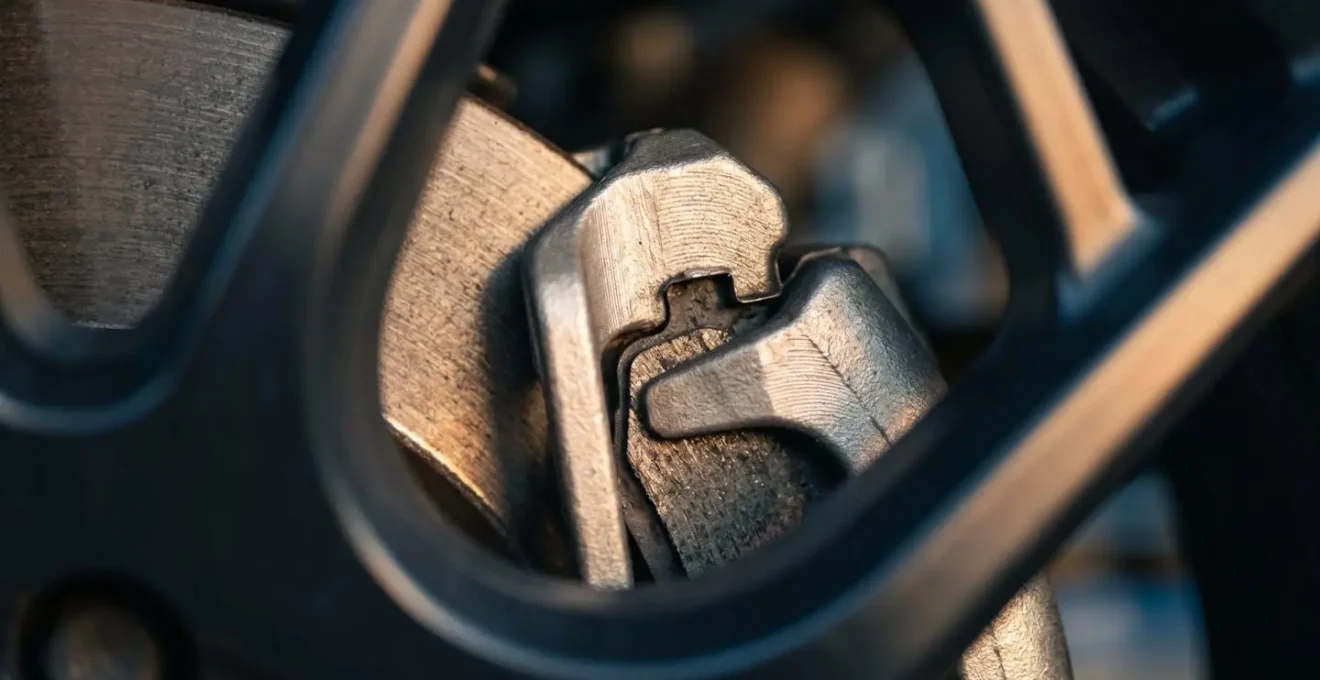 Close-up macro view of brake caliper and disc rotor visible through vehicle alloy wheel spokes with dramatic side lighting