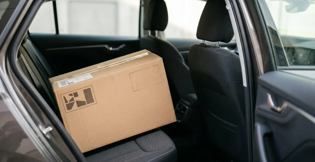 Interior vehicle cargo area showing heavy unsealed cardboard box on rear seat without restraint demonstrating unsafe load